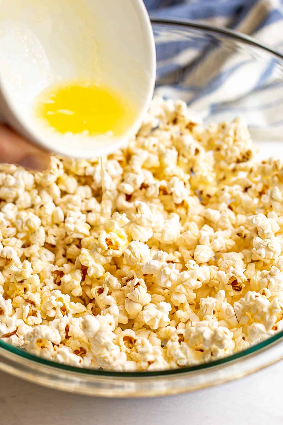 Melted butter being poured over a large bowl of popcorn.