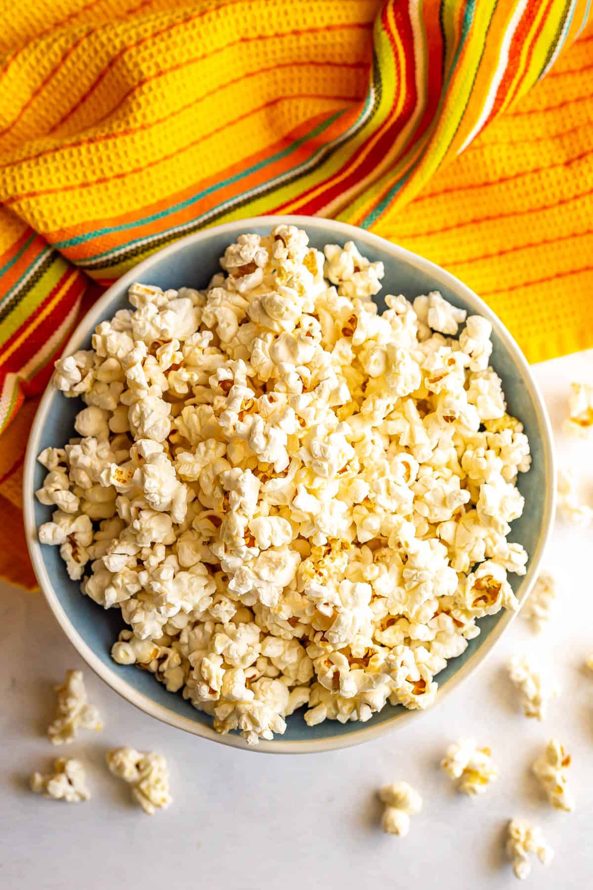 A blue and white bowl filled with popcorn with kernels spilling over onto the counter.