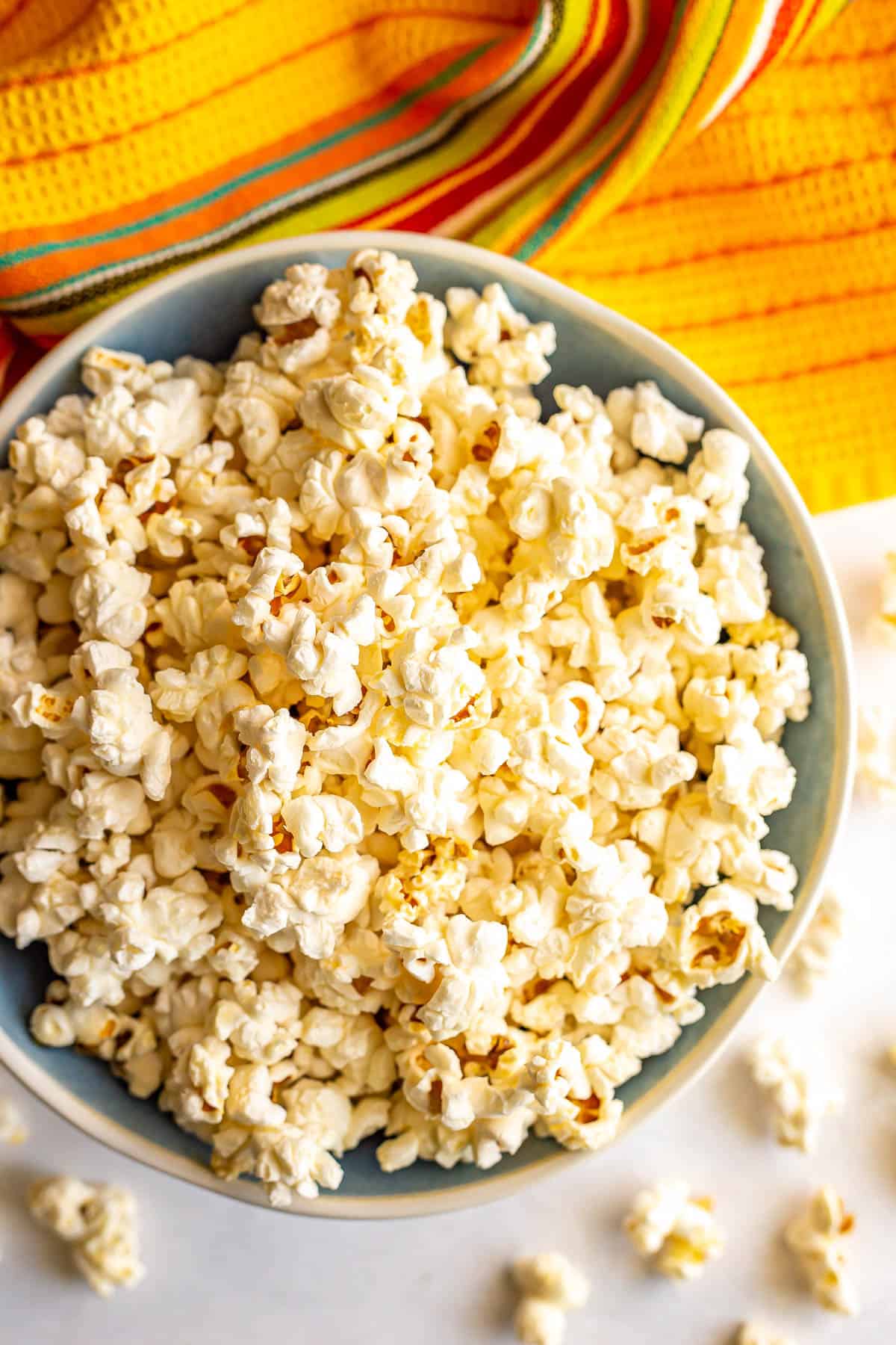 Butter popcorn in a blue and while bowl with some pieces spilling out onto the counter.