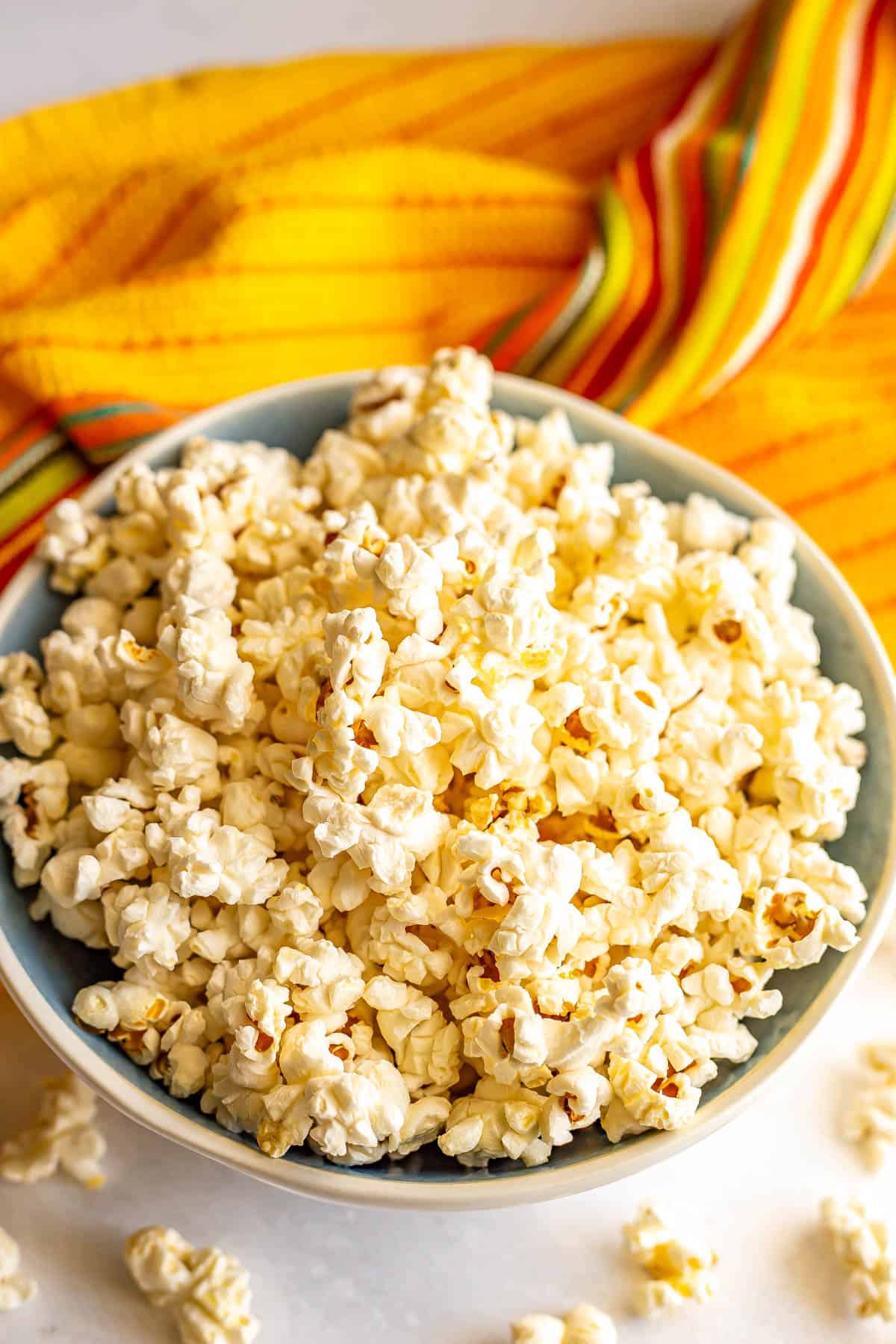 Homemade popcorn served in a blue and white bowl with a colorful yellow throw towel in the background.