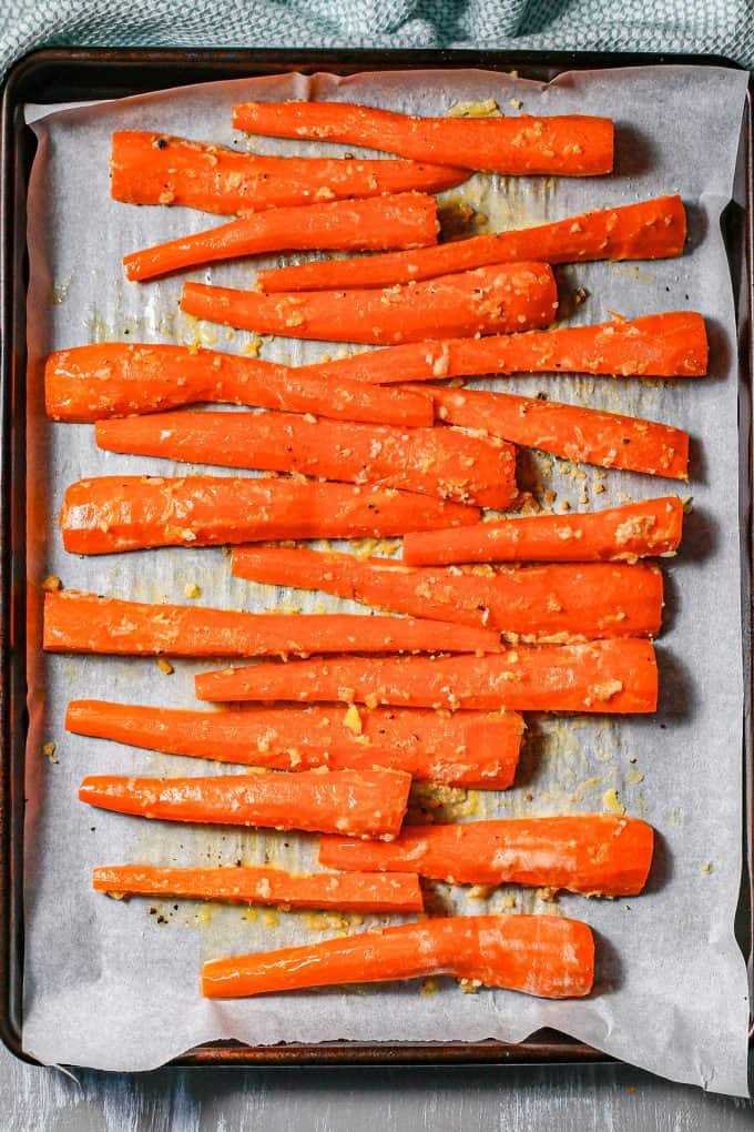 Sliced carrots seasoned with butter and garlic on a parchment paper lined baking sheet.