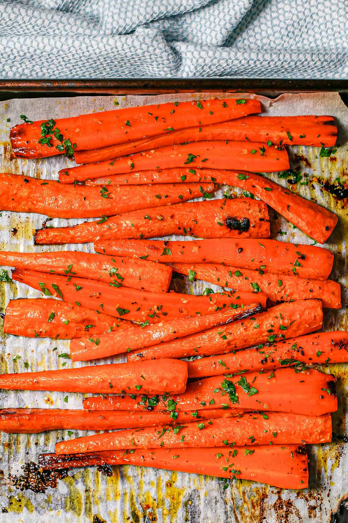 Roasted whole carrots on a parchment paper lined baking sheet after cooking with parsley sprinkled on top.