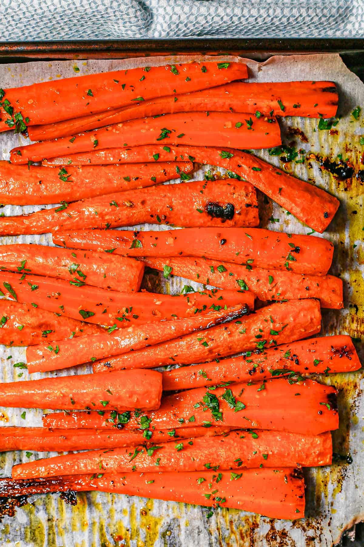 Close up of roasted whole carrots on a parchment paper lined baking sheet after cooking with parsley sprinkled on top.