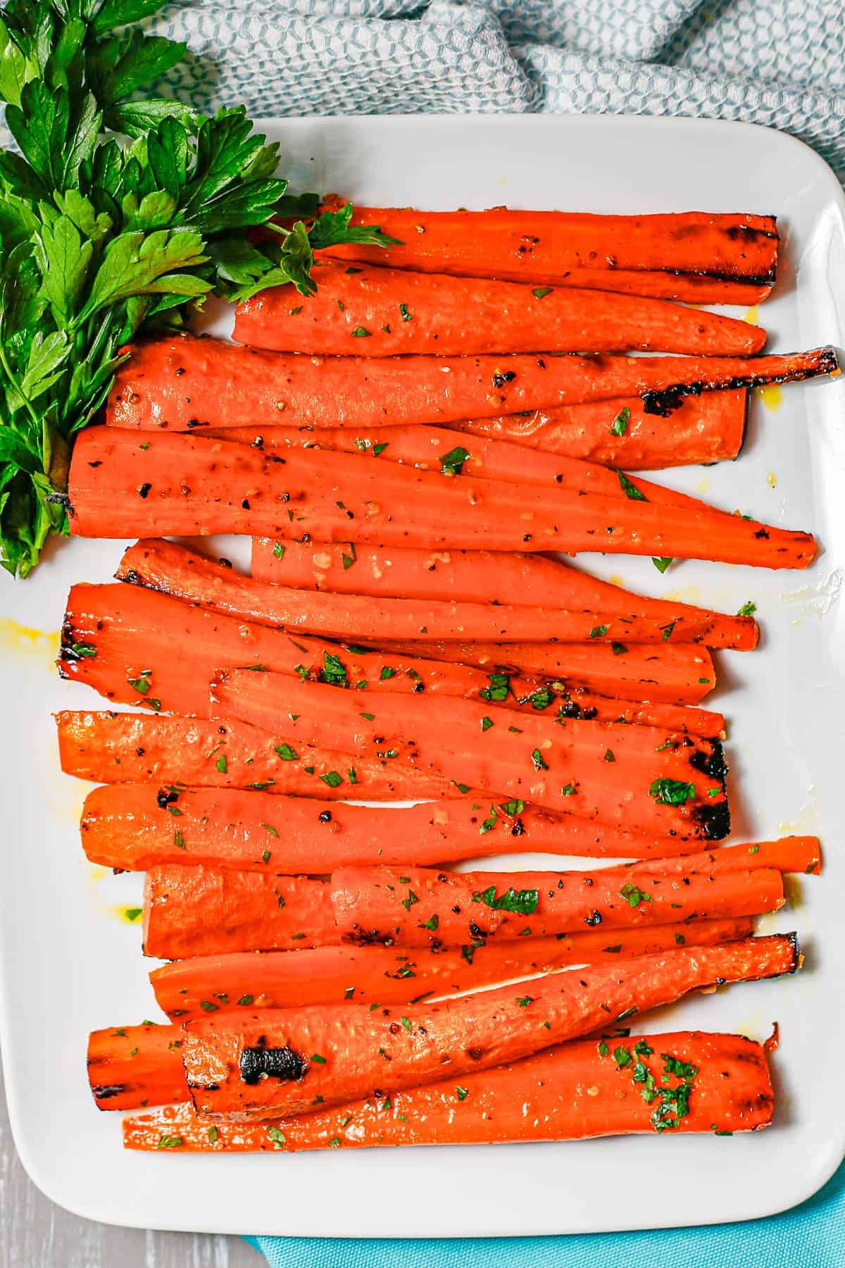 A white rectangular plate with a pile of roasted carrots topped with chopped parsley and a bunch of parsley to the side.