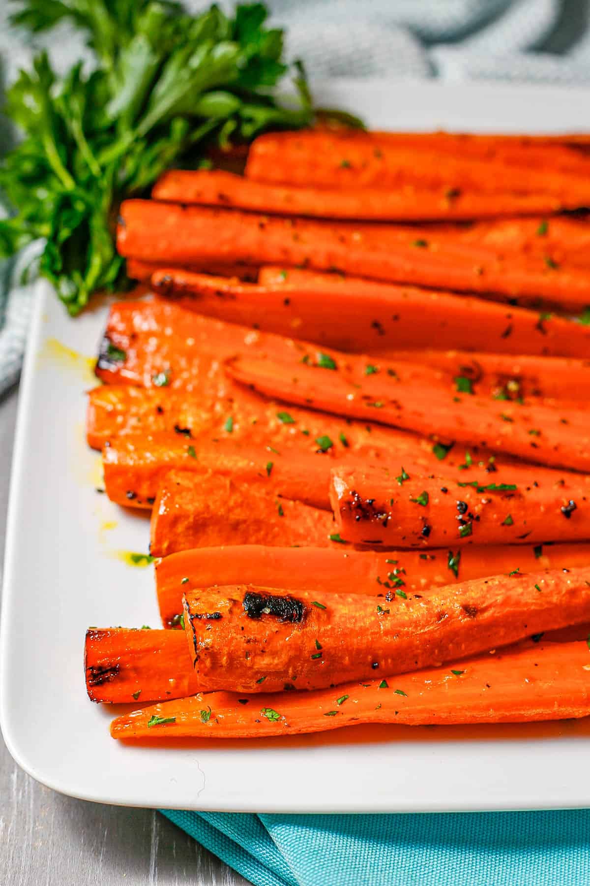 Roasted carrots served on a white rectangular plate with a bunch of parsley as garnish.