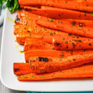 Close up of browned carrots that have been roasted with butter and garlic and served topped with chopped fresh parsley.