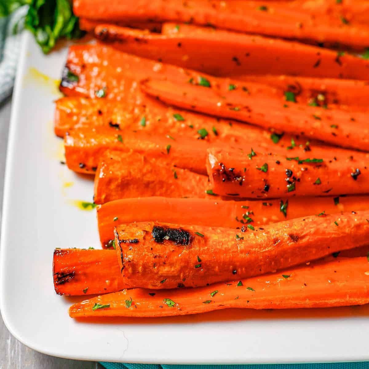 Close up of browned carrots that have been roasted with butter and garlic and served topped with chopped fresh parsley.