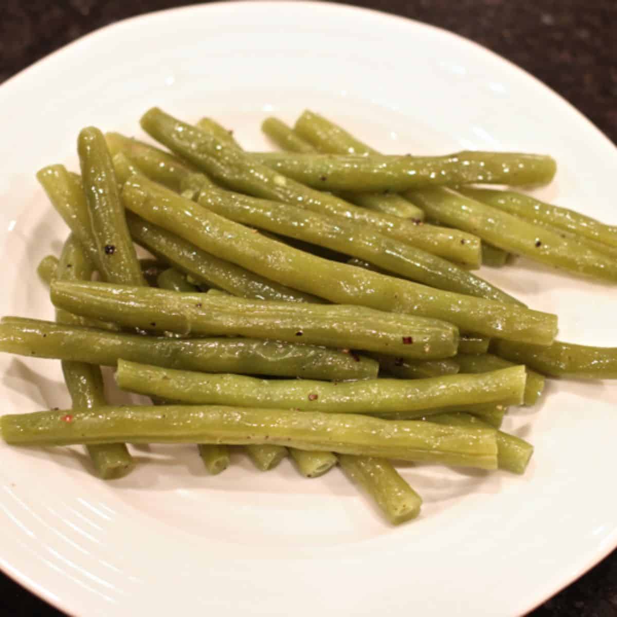 Very tender slow cooked green beans seasoned with butter, salt and pepper served on a small round white plate.