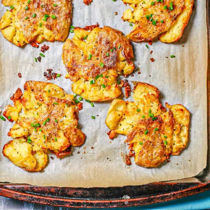 Flattened crispy roasted potatoes on a parchment paper lined baking sheet.