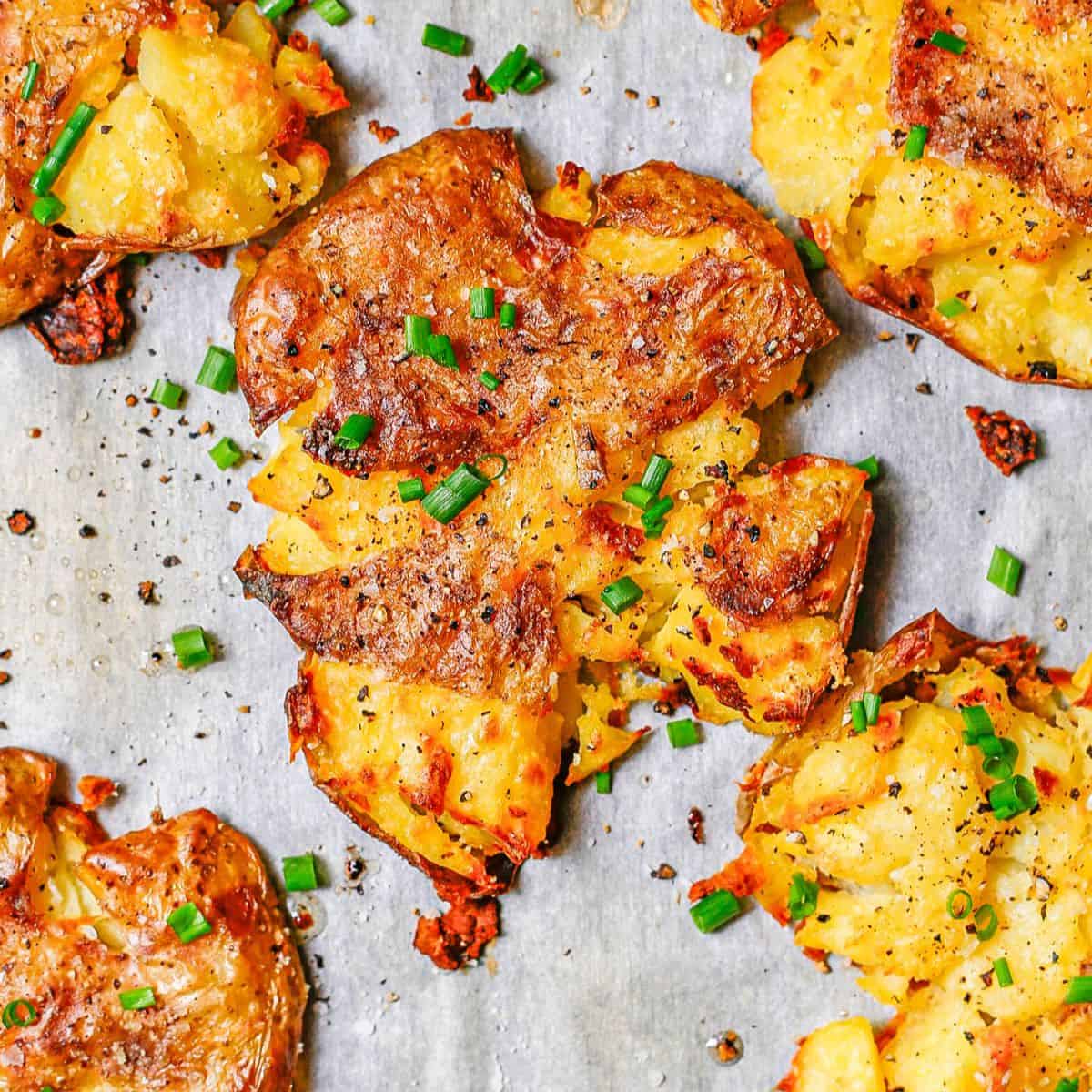 Close up of a crispy roasted Yukon potato that's been smashed onto the parchment paper lined baking sheet and topped with chopped fresh chives.