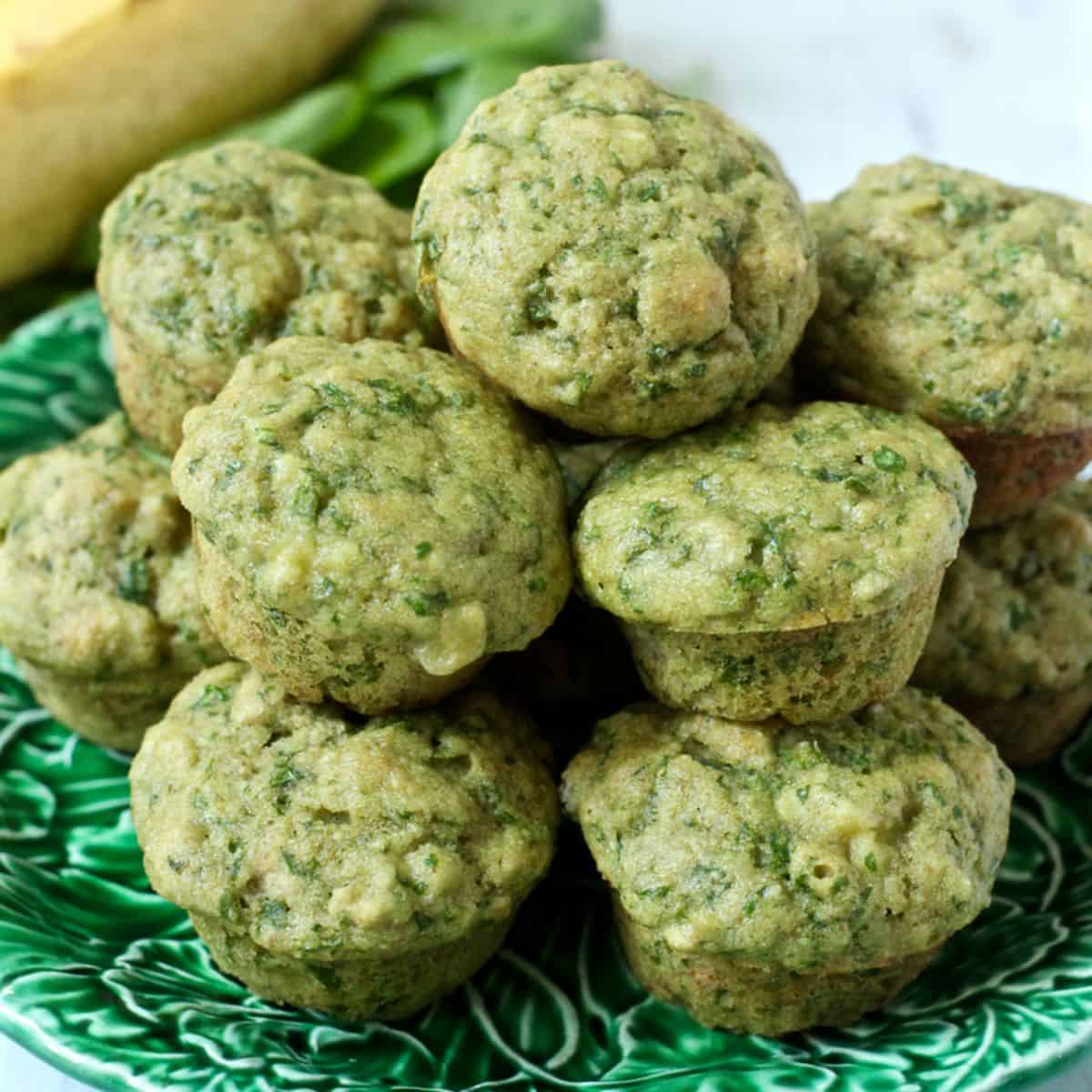 A green plate piled with stacked mini spinach banana muffins.