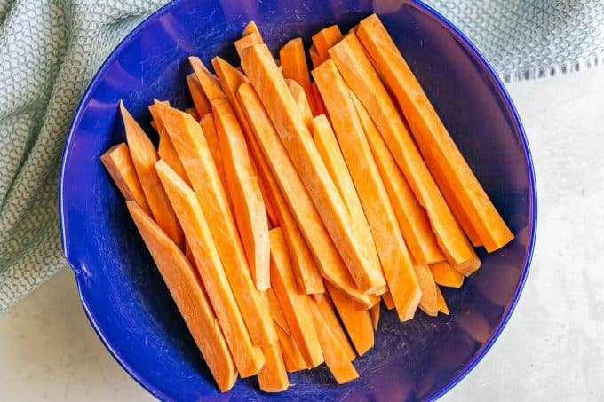 Raw sweet potato cut into fry shape in a large blue bowl.