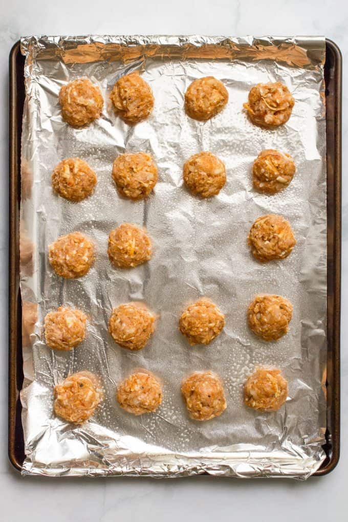 Chicken meatballs with cheese spaced out on a foil lined baking sheet before being cooked.