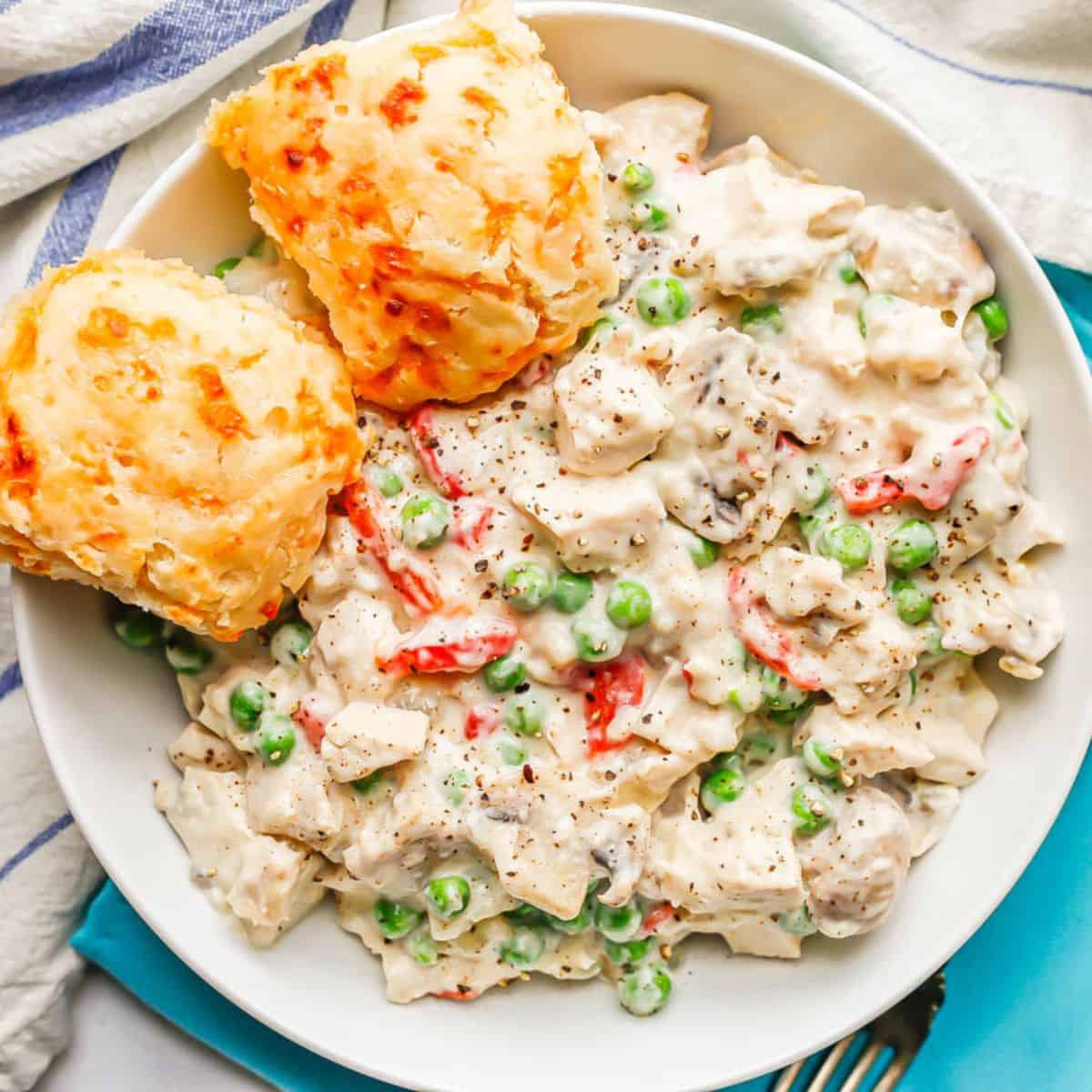 Close up of chicken a la King served in a low white bowl with cheddar biscuits to the side.