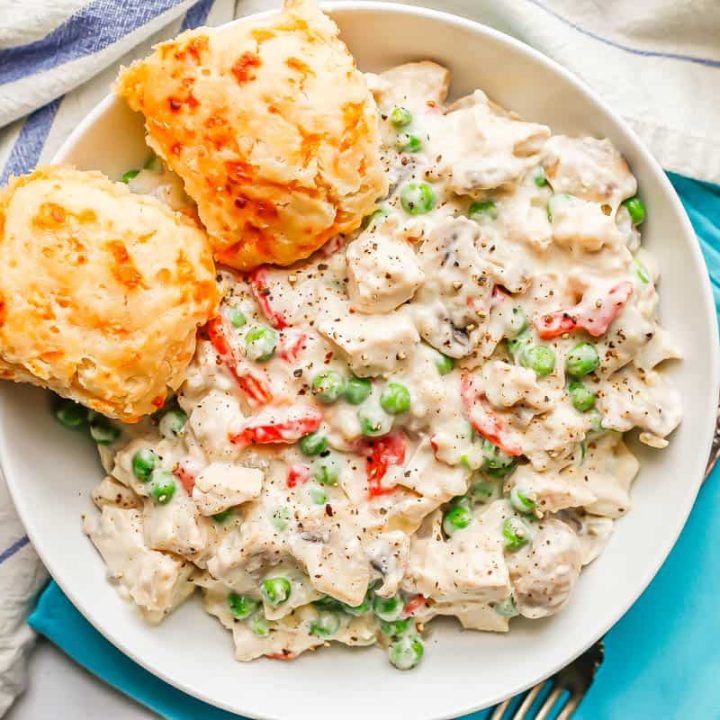 A creamy chicken dish with mushrooms, peas and pimientos served in a white bowl with two cheddar biscuits to the side.
