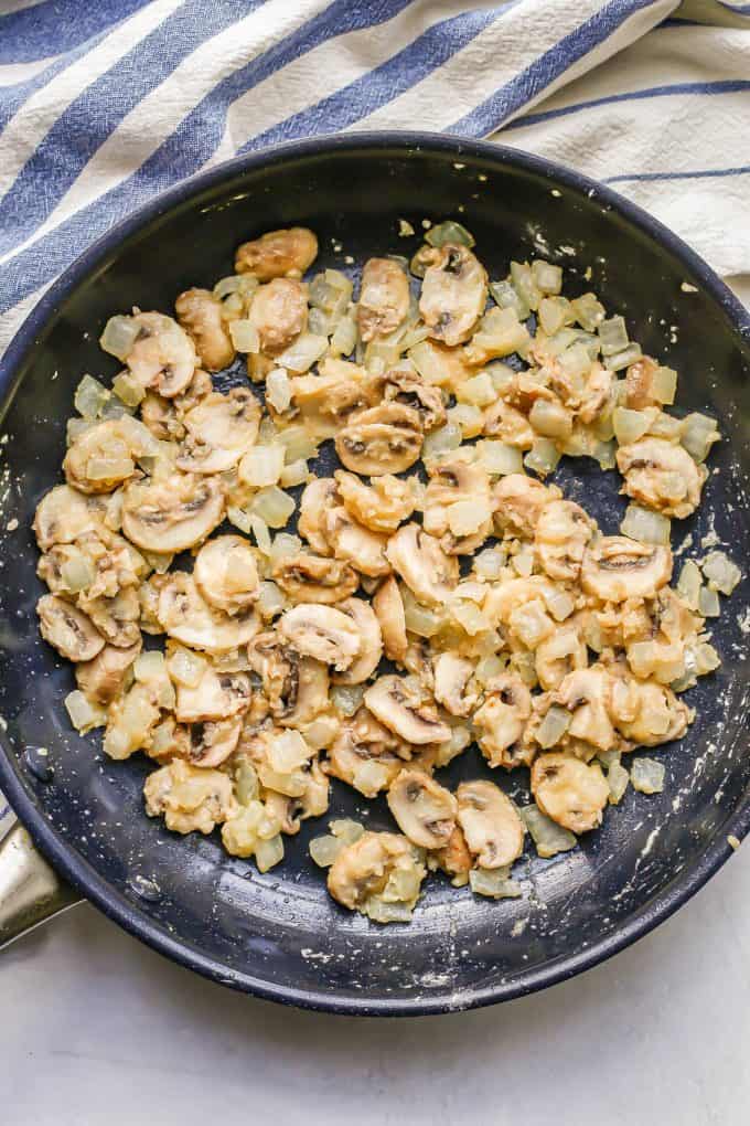 Sautéed onion and mushrooms coated in flour in a large dark skillet.