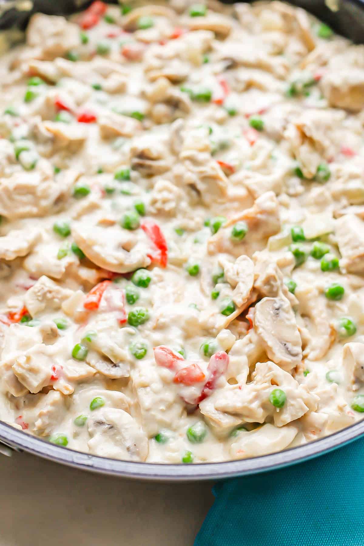 Close up of a creamy chicken mixture in a large dark skillet with mushrooms, green peas and pimientos.