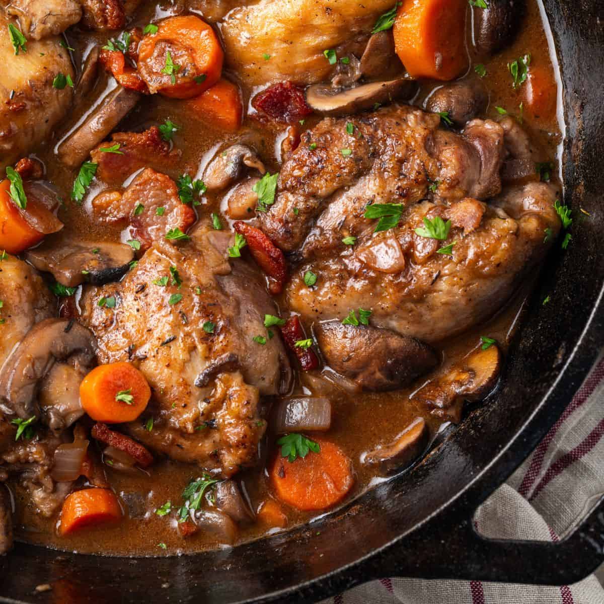 Close up of seared chicken with veggies in a cast iron pan with parsley sprinkled on top.