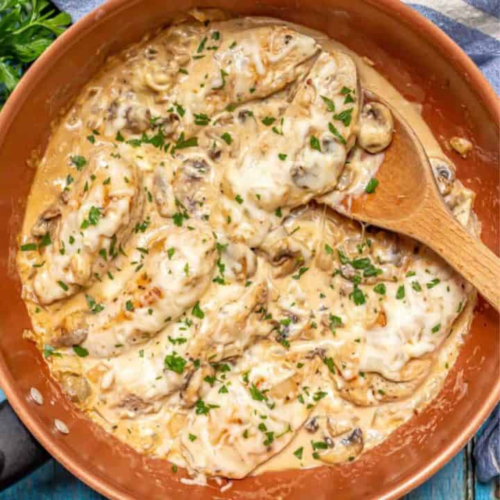 A cream cheese chicken and mushroom mixture in a large pan with a wooden spoon resting in it.