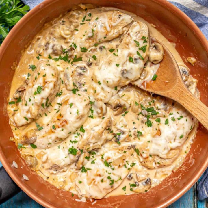 A cream cheese chicken and mushroom mixture in a large pan with a wooden spoon resting in it.
