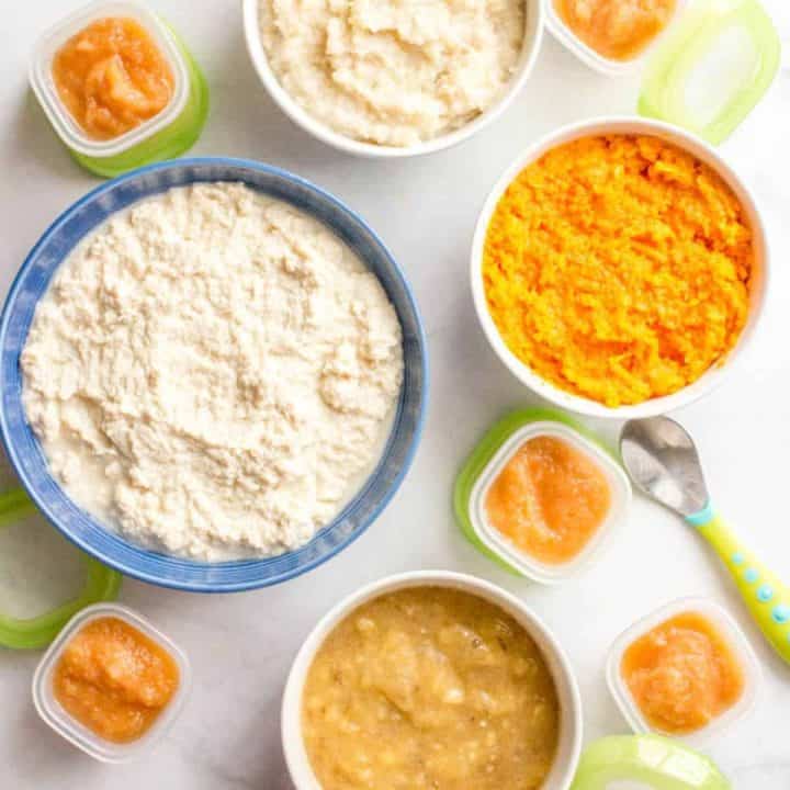 A collection of bowls and small containers with homemade baby food of sweet potatoes, brown rice, chicken, pears and banana purees.