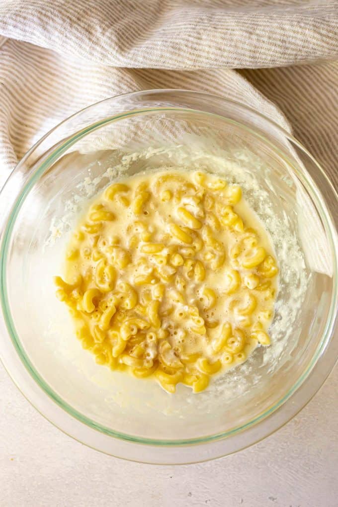 Mac and cheese ingredients stirred together in a large glass bowl before being cooked in the microwave.