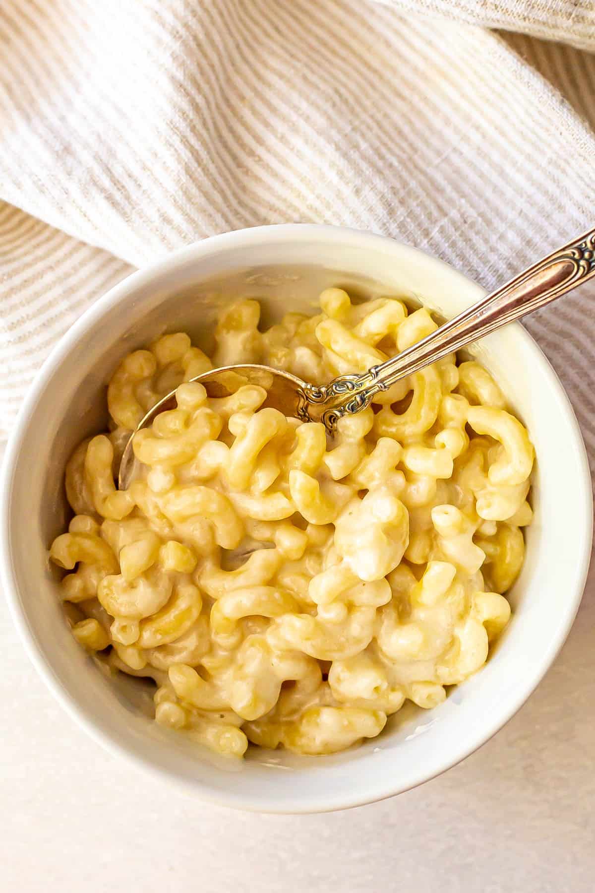Close up of microwave mac and cheese served in a small white bowl with a spoon resting in it.