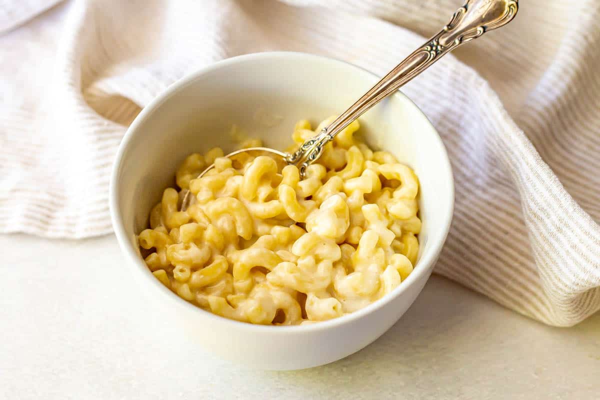 A spoon resting in a small white bowl of microwave mac and cheese.