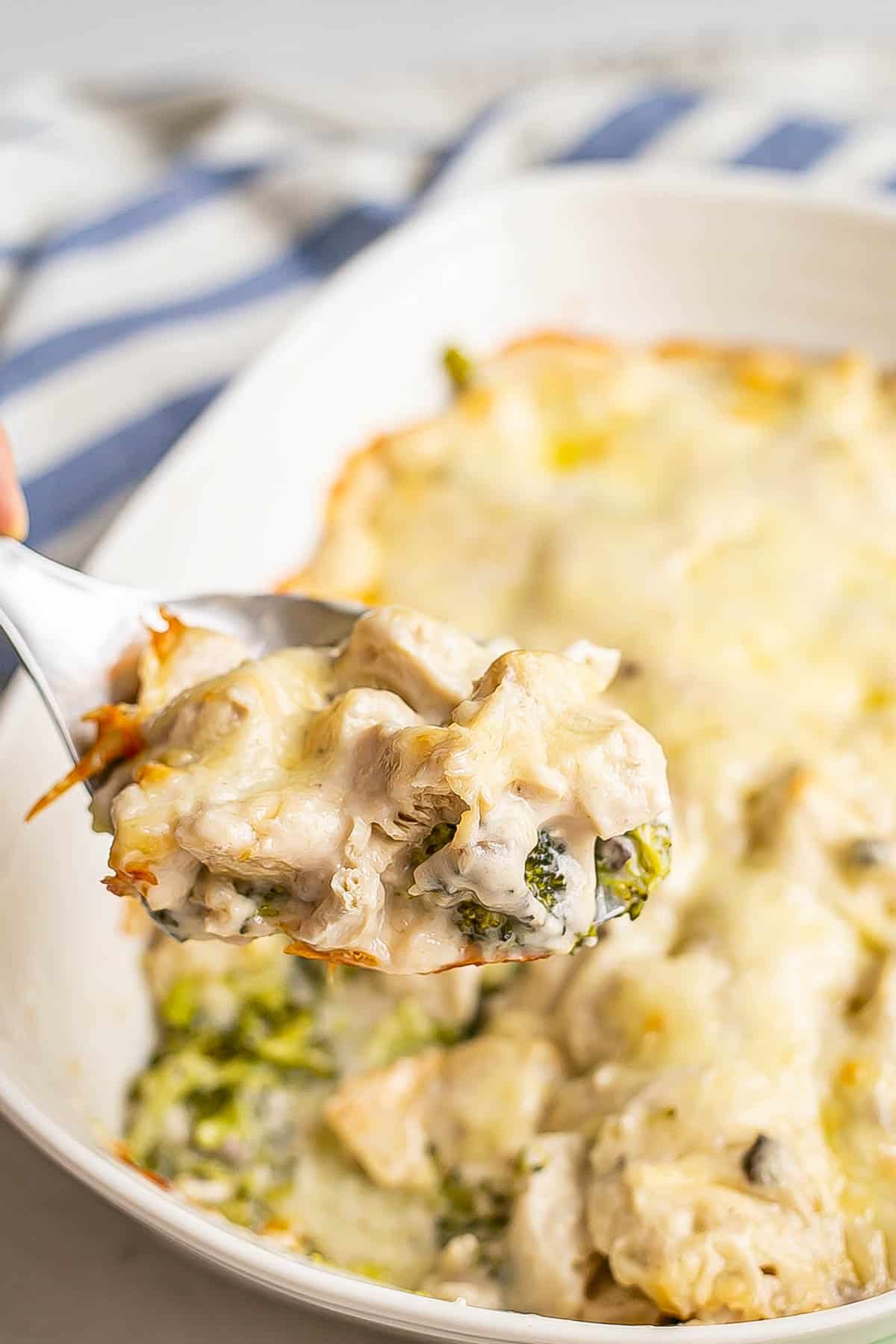 A serving spoon scooping up chicken divan from a white casserole dish.