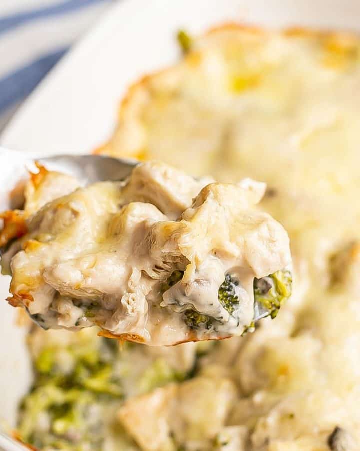 Close up of a serving spoon scooping up chicken divan from a white casserole dish.