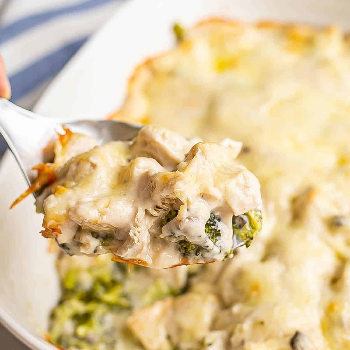 Close up of a serving spoon scooping up chicken divan from a white casserole dish.