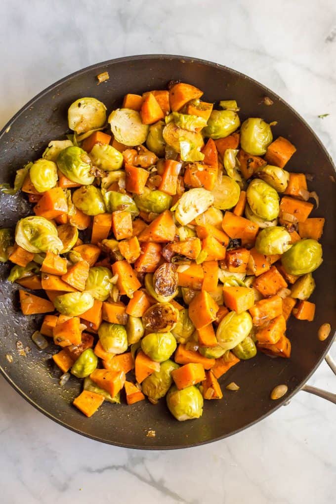 A large dark skillet with a mixture of sautéed veggies, including brussels sprouts and sweet potatoes.