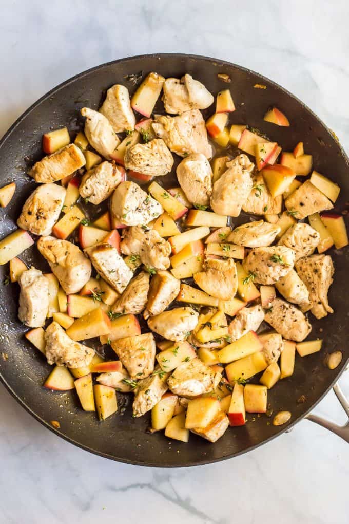 Sautéed chicken and apples with thyme in a large dark skillet.