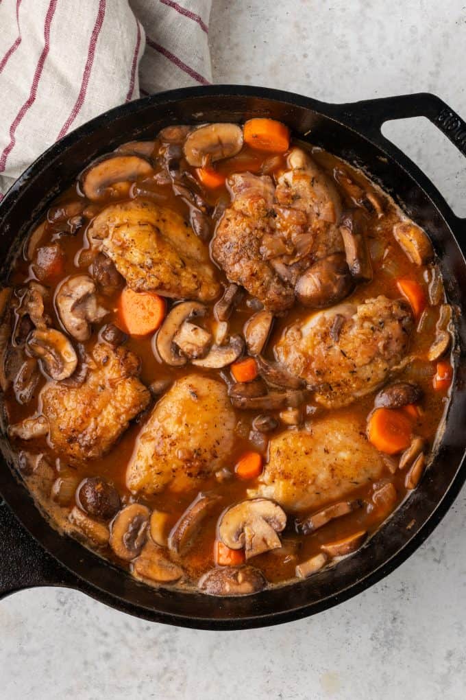 Coq au vin simmering in a cast iron pan.