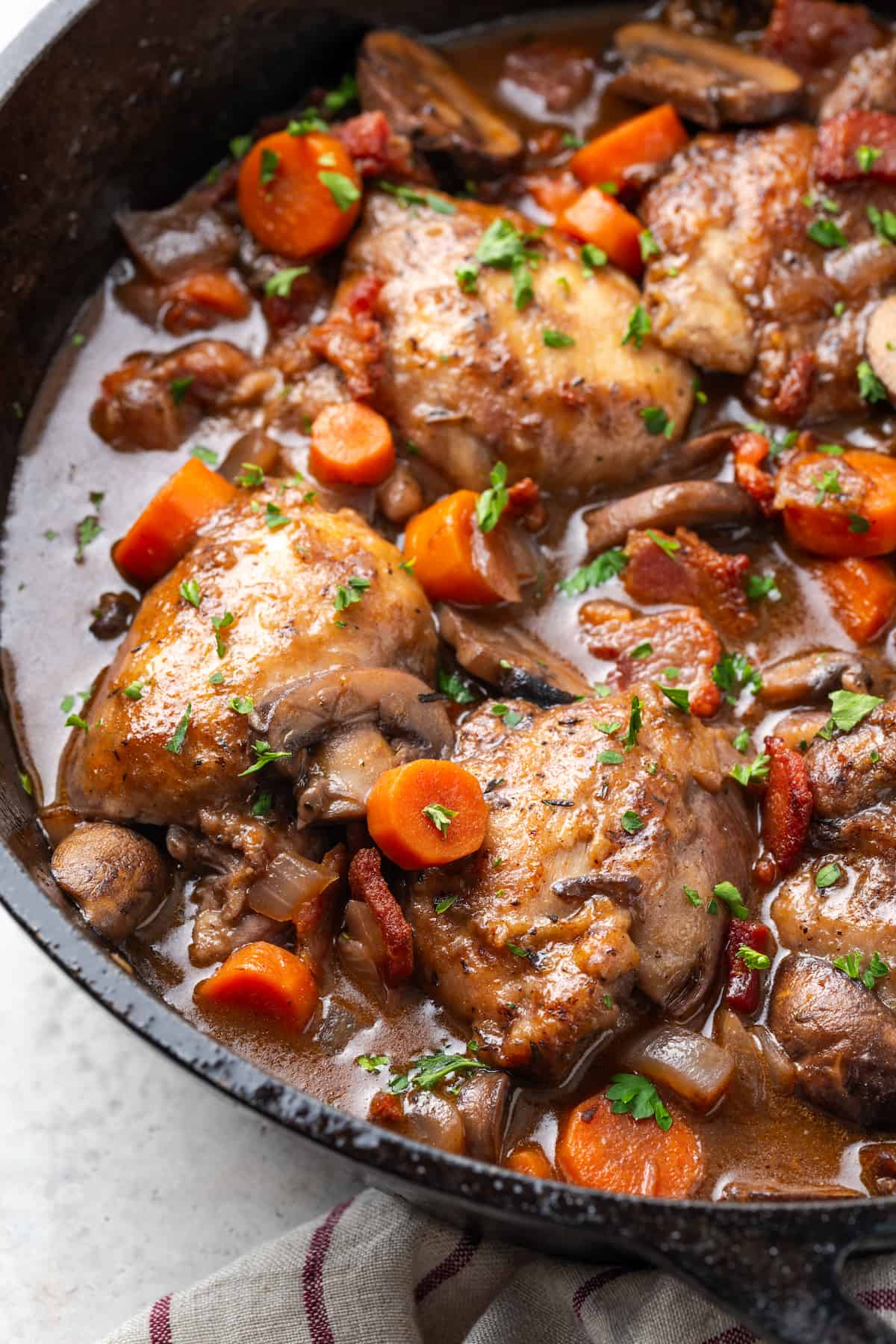 Coq au vin with carrots and mushrooms in a red wine sauce in a cast iron skillet.