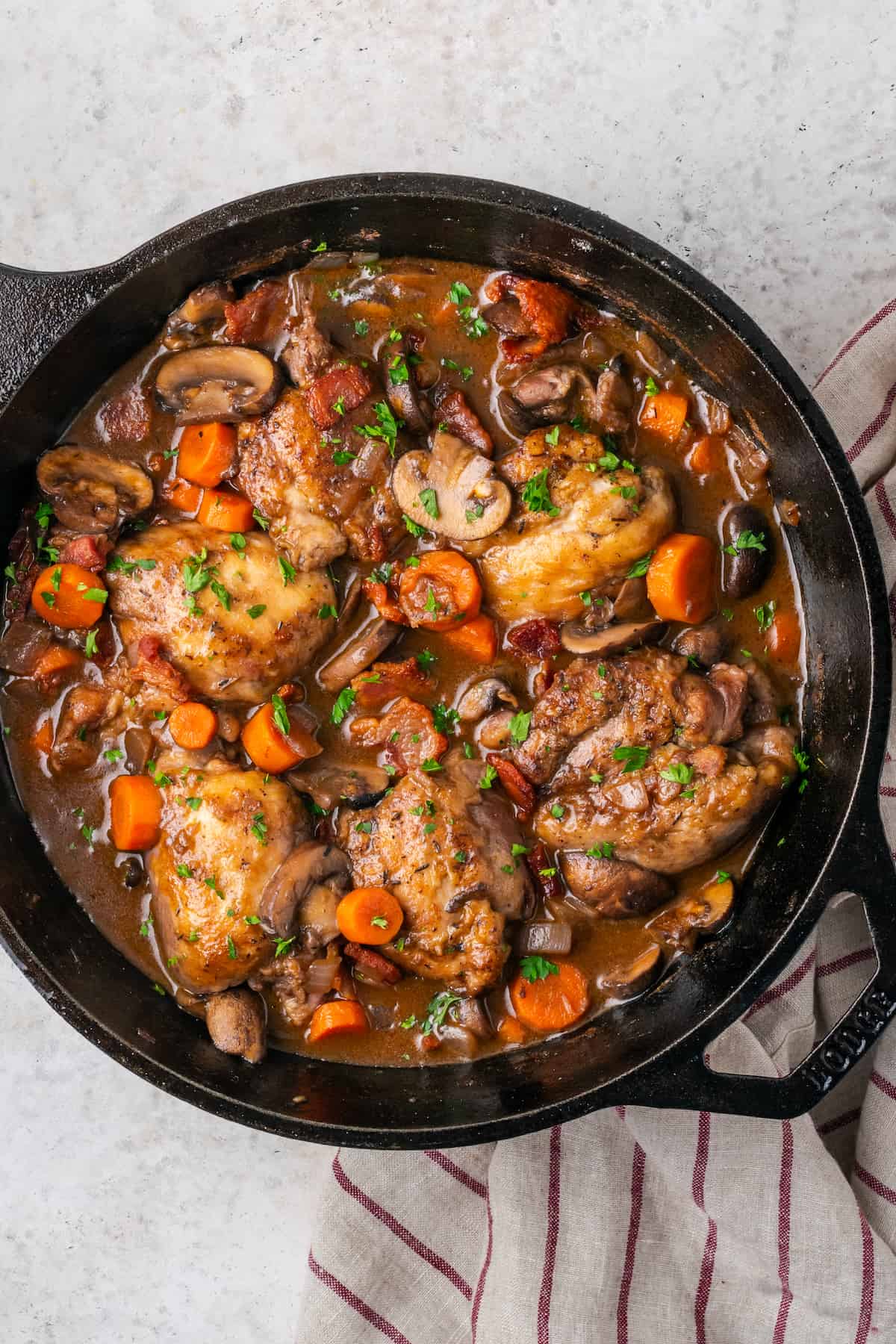 A cast iron skillet with a finished coq au vin dish sprinkled with parsley.