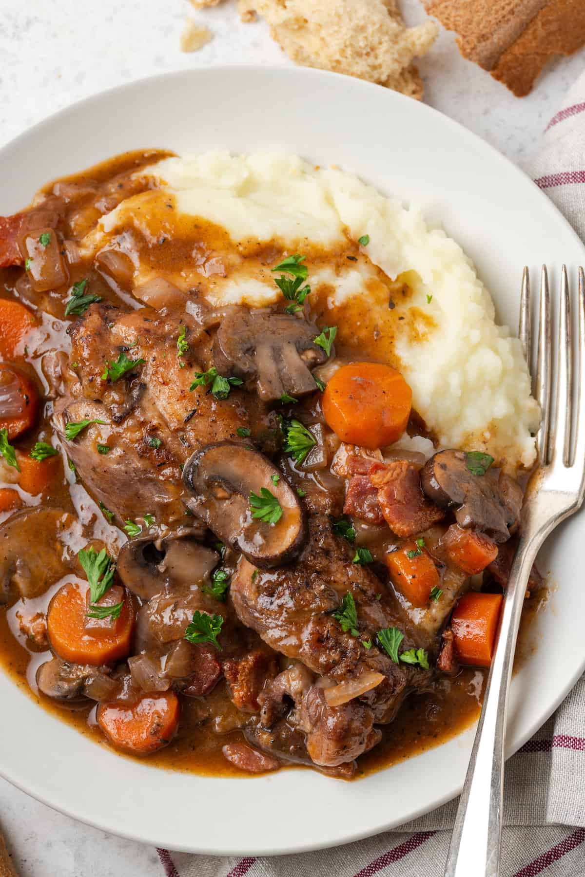 Coq au vin served over mashed potatoes on a white plate with a fork resting on the side.