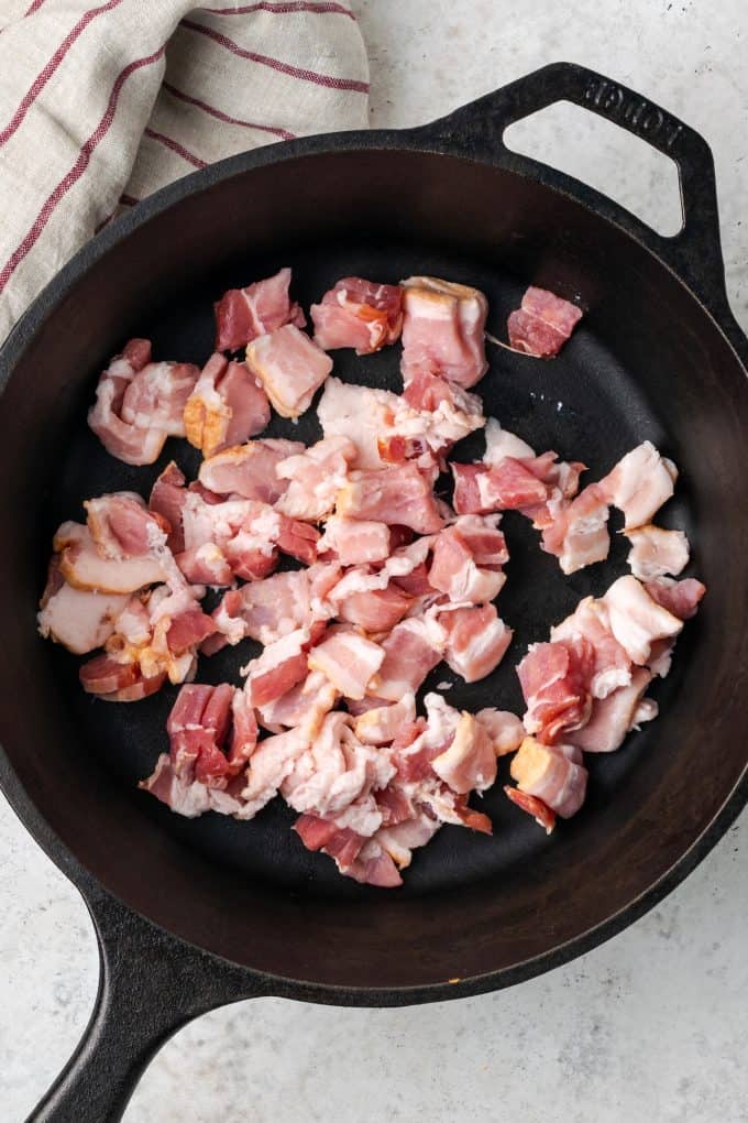 Cut bacon pieces being added to a cast iron pan.