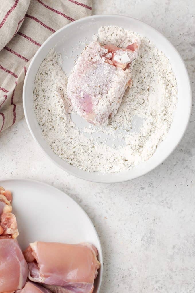 A chicken thigh being dredged in a flour mixture.