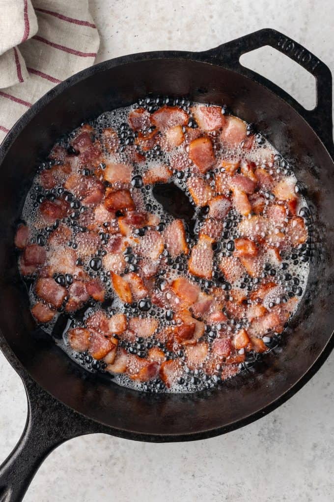 Cooked bacon pieces and grease in a cast iron pan.