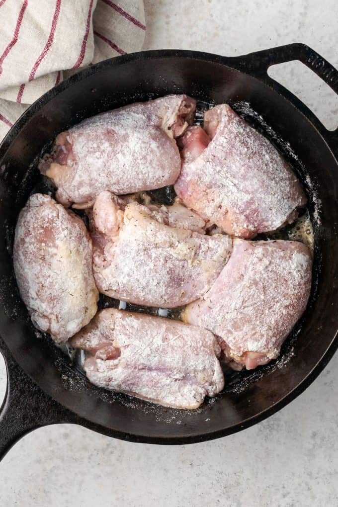 Chicken thighs coated in flour nestled into a cast iron pan.