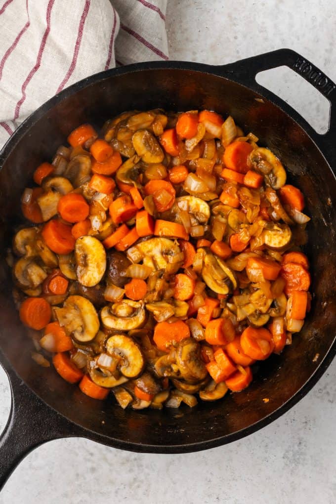 A sautéed mixture of carrots, onions and mushrooms in a cast iron pan.