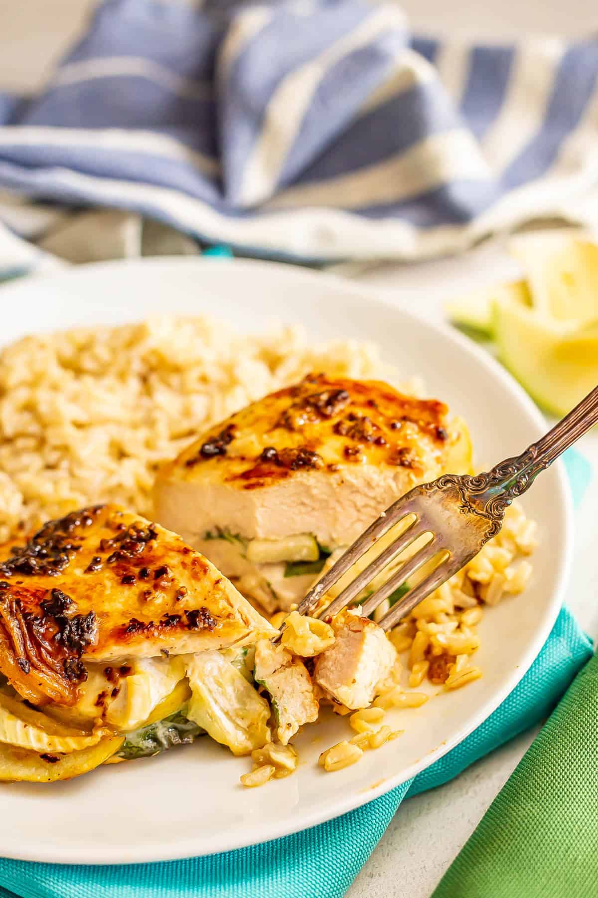A fork picking up a bite of apple brie stuffed chicken from a white dinner plate.