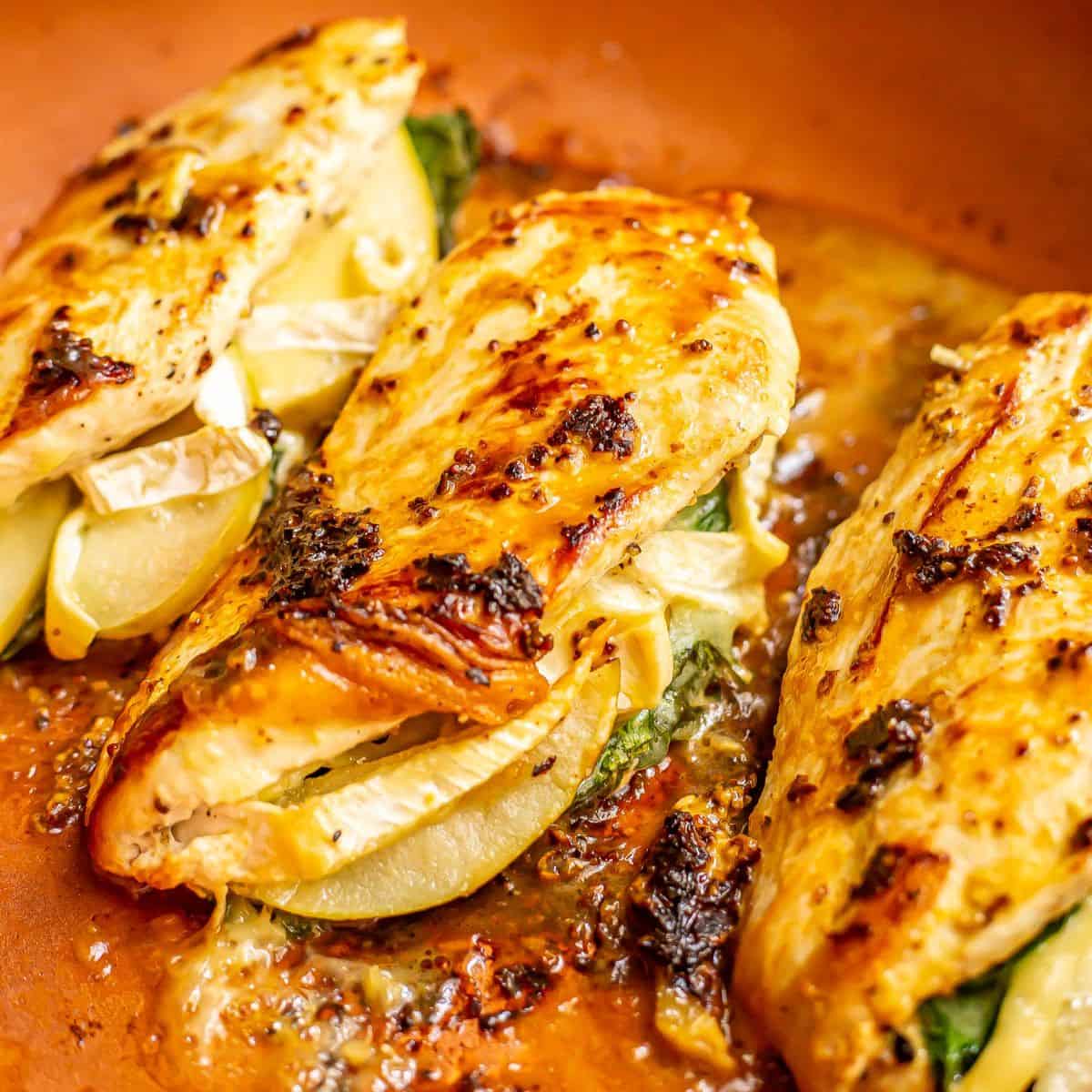 Close up of seared mustard brushed apple brie stuffed chicken breasts in a copper skillet.