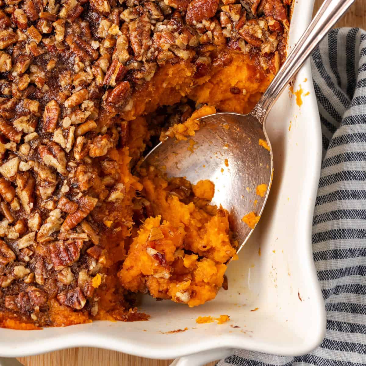 Close up of a bourbon sweet potato casserole with a scoop taken out and a spoon resting in the dish.