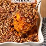 A spoon holding up a scoop of bourbon sweet potato casserole with a nutty streusel topping from a white casserole dish with a text overlay on the photo.
