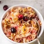 A white round bowl of a winter fruit salad with a spoon resting in it and a text overlay on the photo.