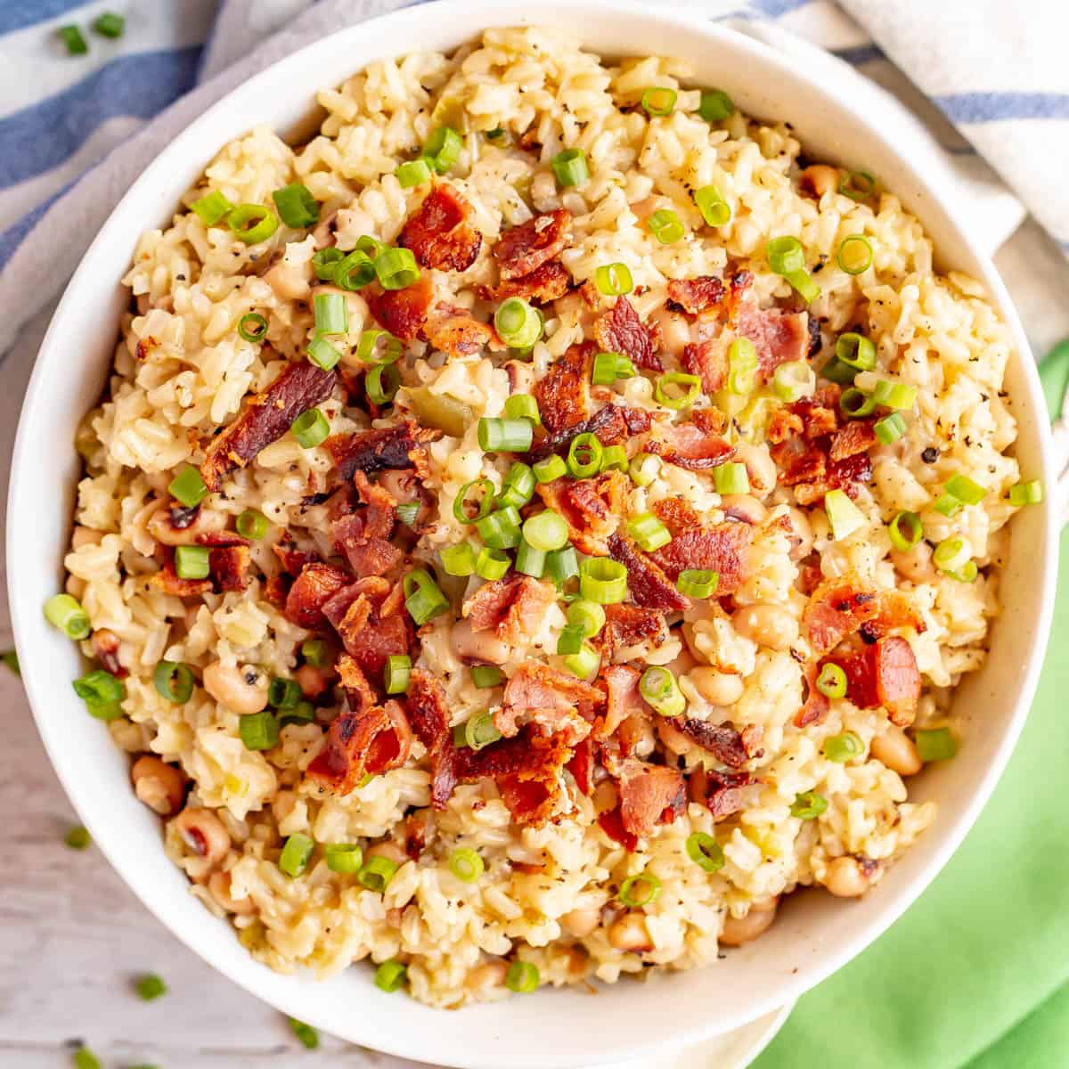 Close up of a large white serving bowl full of hoppin' John with black and sliced green onions on top.