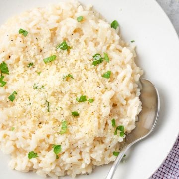 Close up of a spoon resting in a creamy risotto mixture served in a large white bowl.