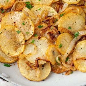 Close up of sliced browned potatoes with onions and chopped fresh parsley on top.